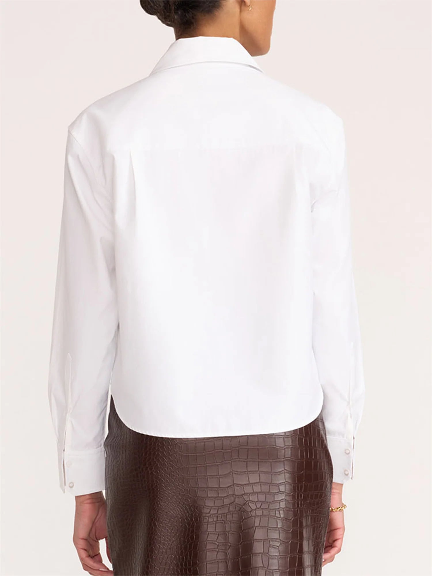 A woman shown from the back wearing a white long-sleeve button-up shirt and a brown crocodile-embossed skirt, against a plain light beige background.