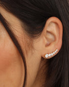 A close-up of a person's ear wearing a curved row of small clear gemstone stud earrings in a silver-toned setting.