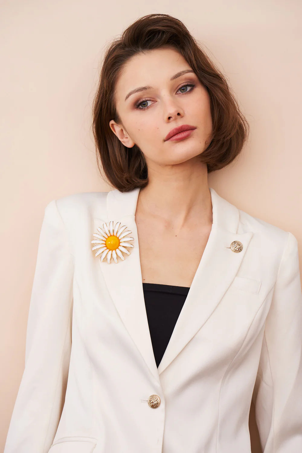 Woman wearing a white blazer with a sunflower brooch against a beige background