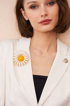 Woman wearing a white blazer with a sunflower brooch against a beige background
