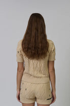 Woman wearing a beige knit outfit with cable patterns on a plain background