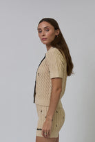 Woman wearing a beige knitted outfit against a plain background
