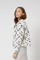 Woman wearing a white jacket with blue floral patterns on a plain background