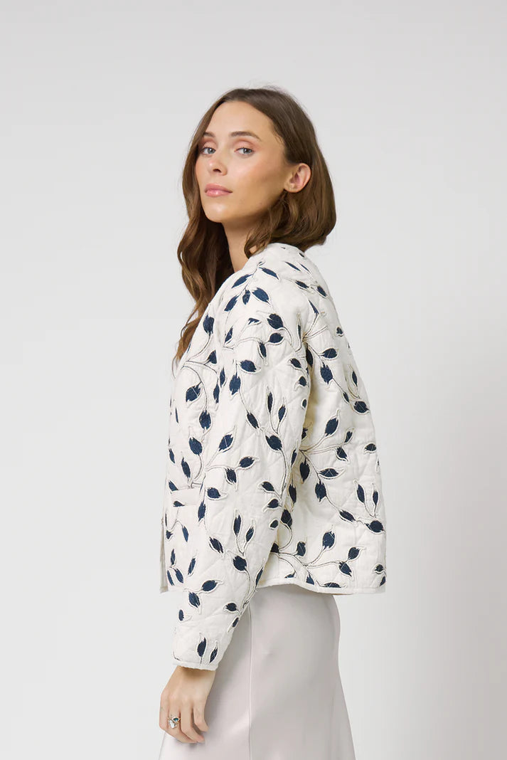 Woman wearing a white jacket with blue floral patterns on a plain background