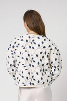 Woman wearing a white floral patterned jacket on a plain background