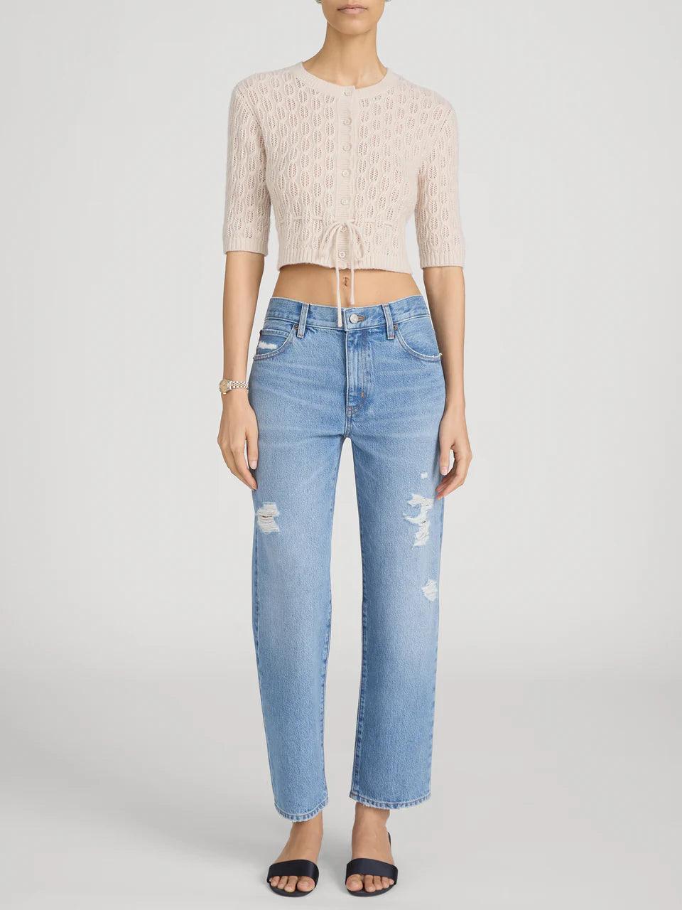 Person wearing a beige cropped sweater and light blue jeans on a white background