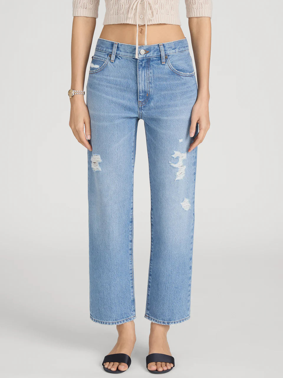 Person wearing light blue distressed jeans on a white background