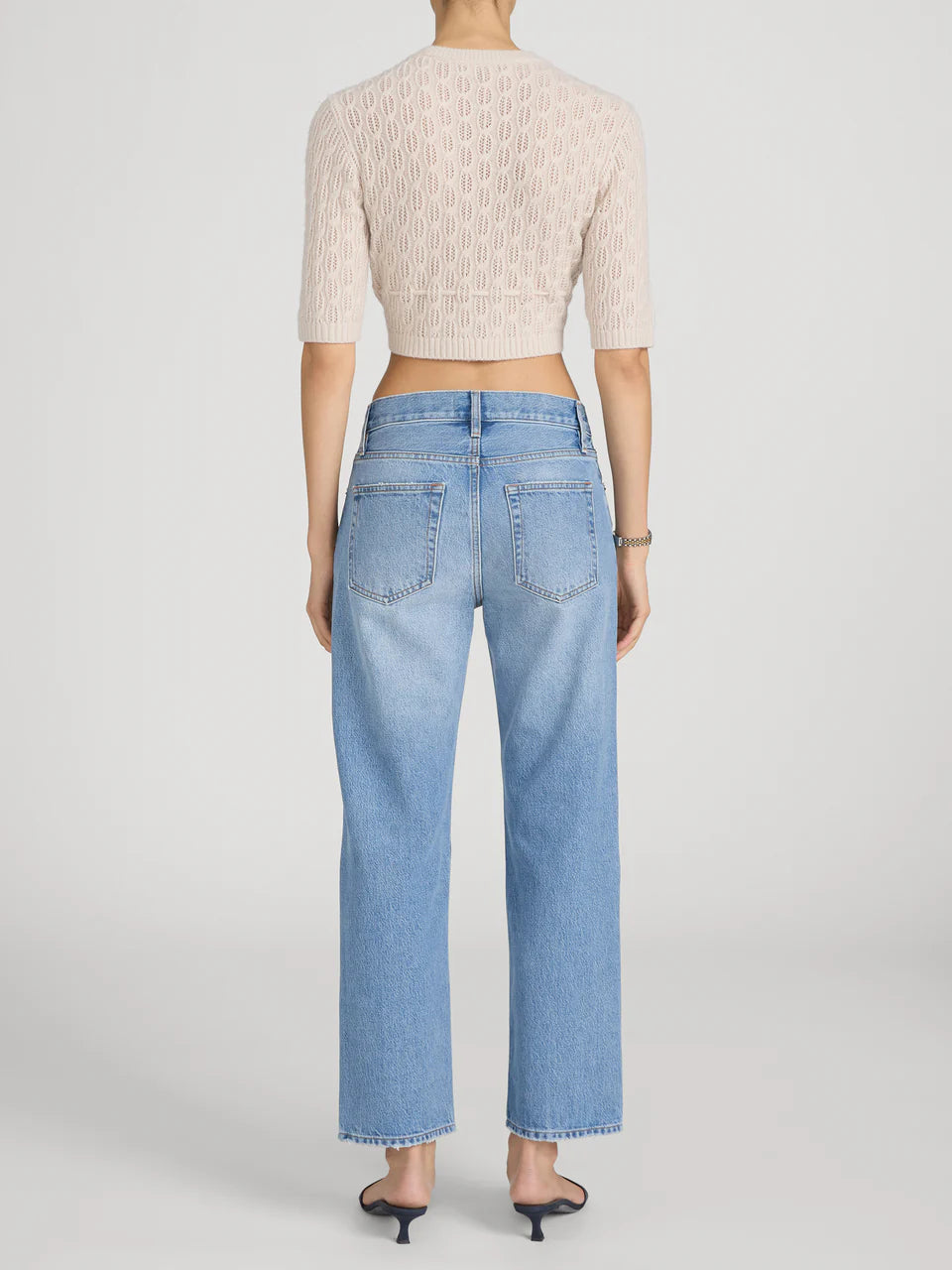 Person wearing light blue jeans and a beige cropped sweater on a plain background