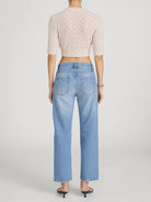 Person wearing light blue jeans and a beige cropped sweater on a plain background