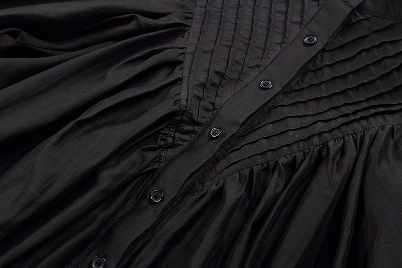 Close-up of a black pleated dress with buttons on a dark background