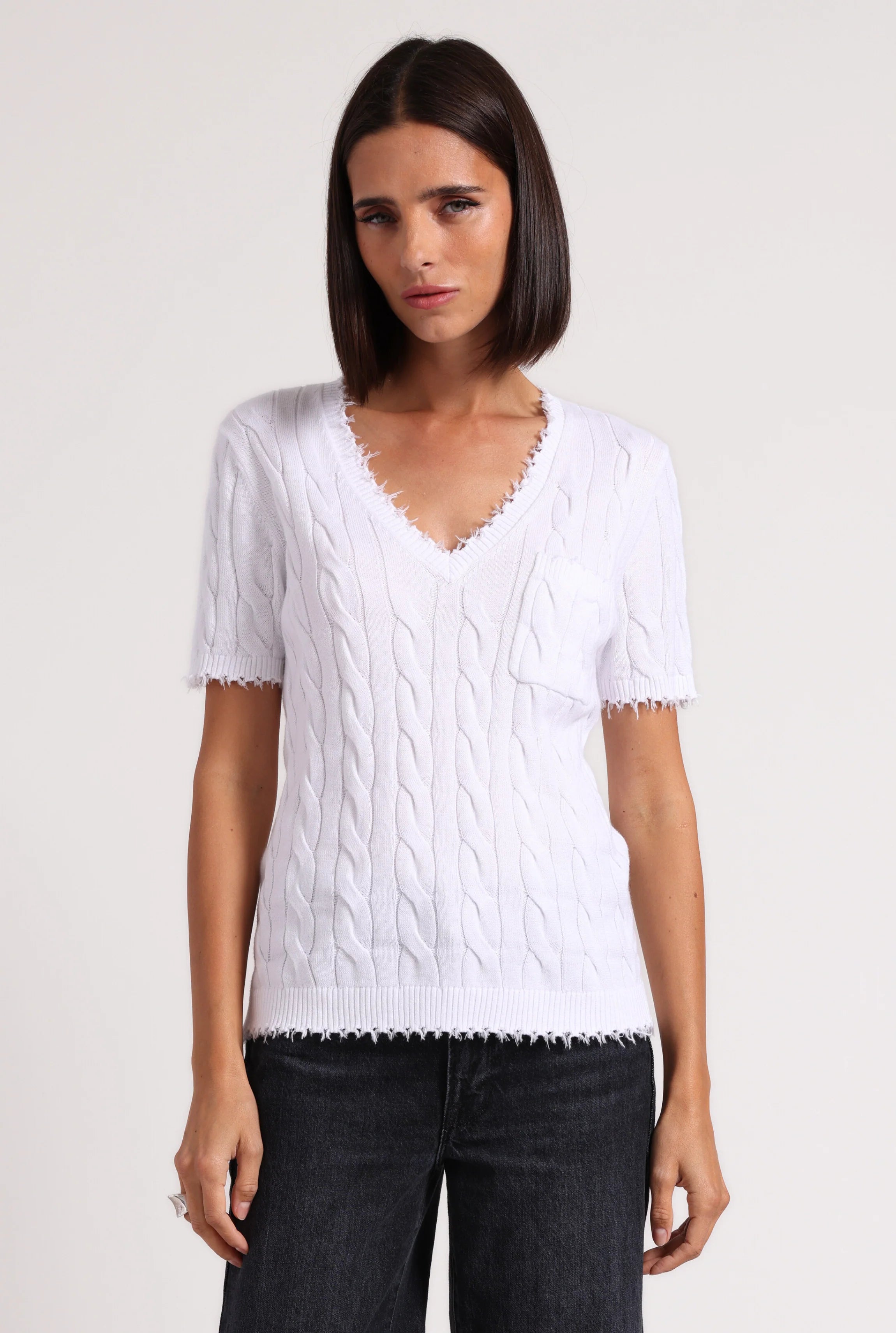 Woman wearing a white cable knit sweater with black pants on a plain background