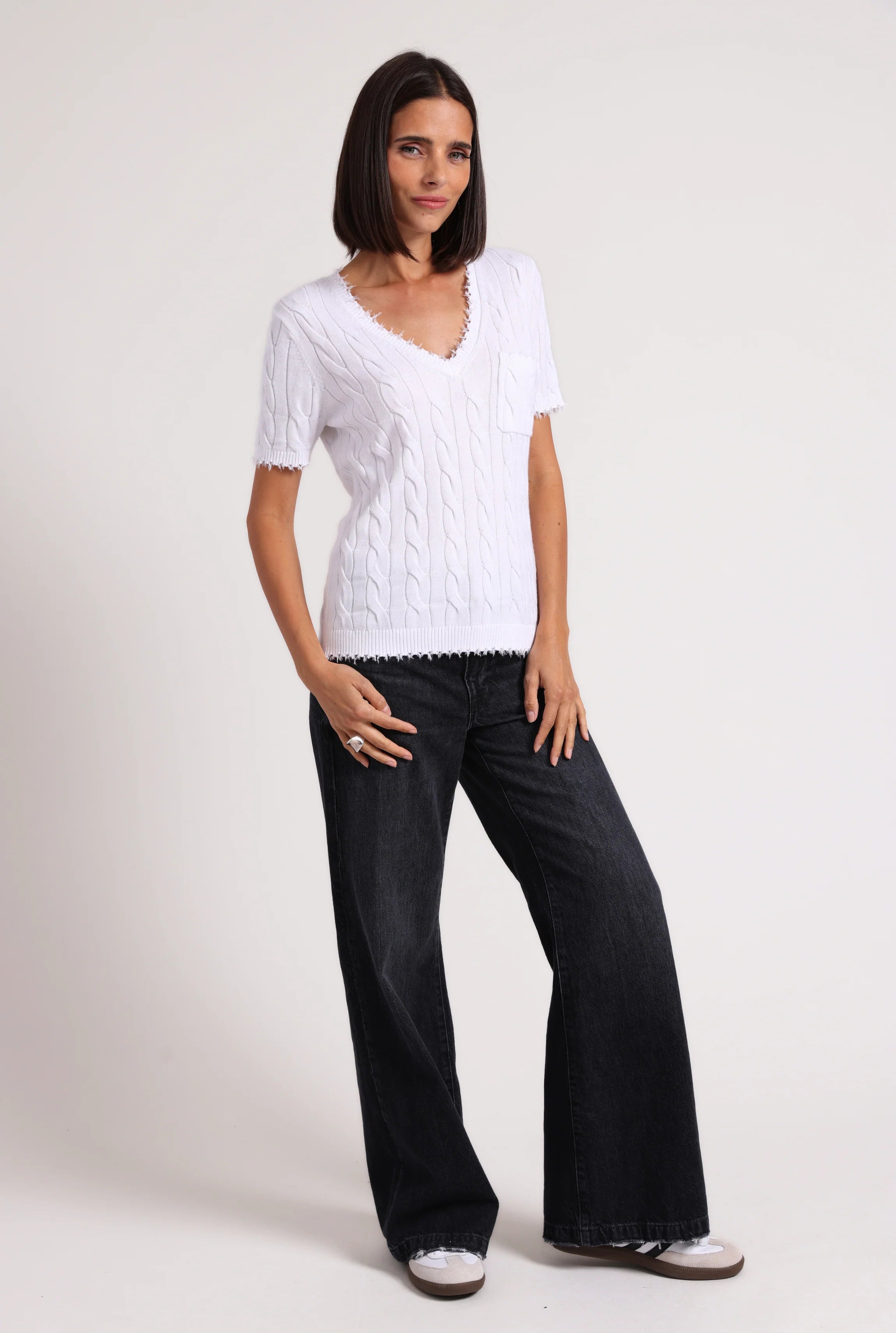 Woman wearing a white sweater and black pants on a plain background