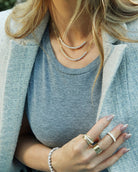 Person wearing layered necklaces, a ring, and a bracelet with a neutral background