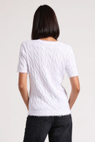 Person wearing a white cable knit sweater on a plain background