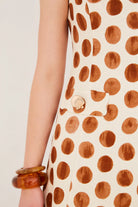 Close-up of a sleeveless dress with brown polka dot pattern on a plain background