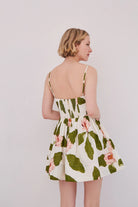 Woman wearing a floral dress with green leaves and pink flowers on a plain background