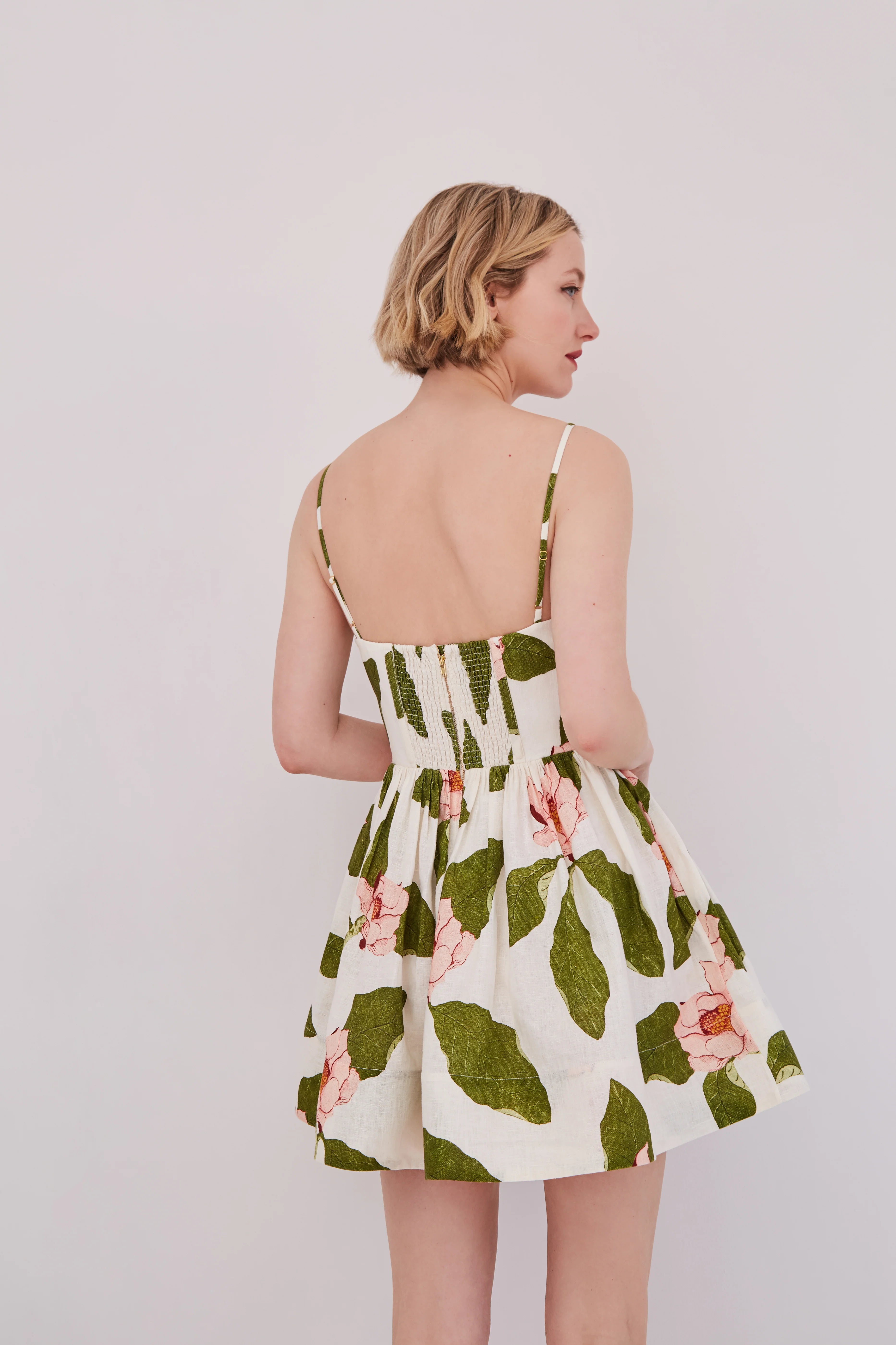 Woman wearing a floral dress with green leaves and pink flowers on a plain background
