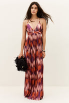 Woman wearing a patterned dress holding a black clutch against a white background