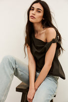Woman wearing a black off-shoulder top and light blue jeans sitting on a wooden stool.
