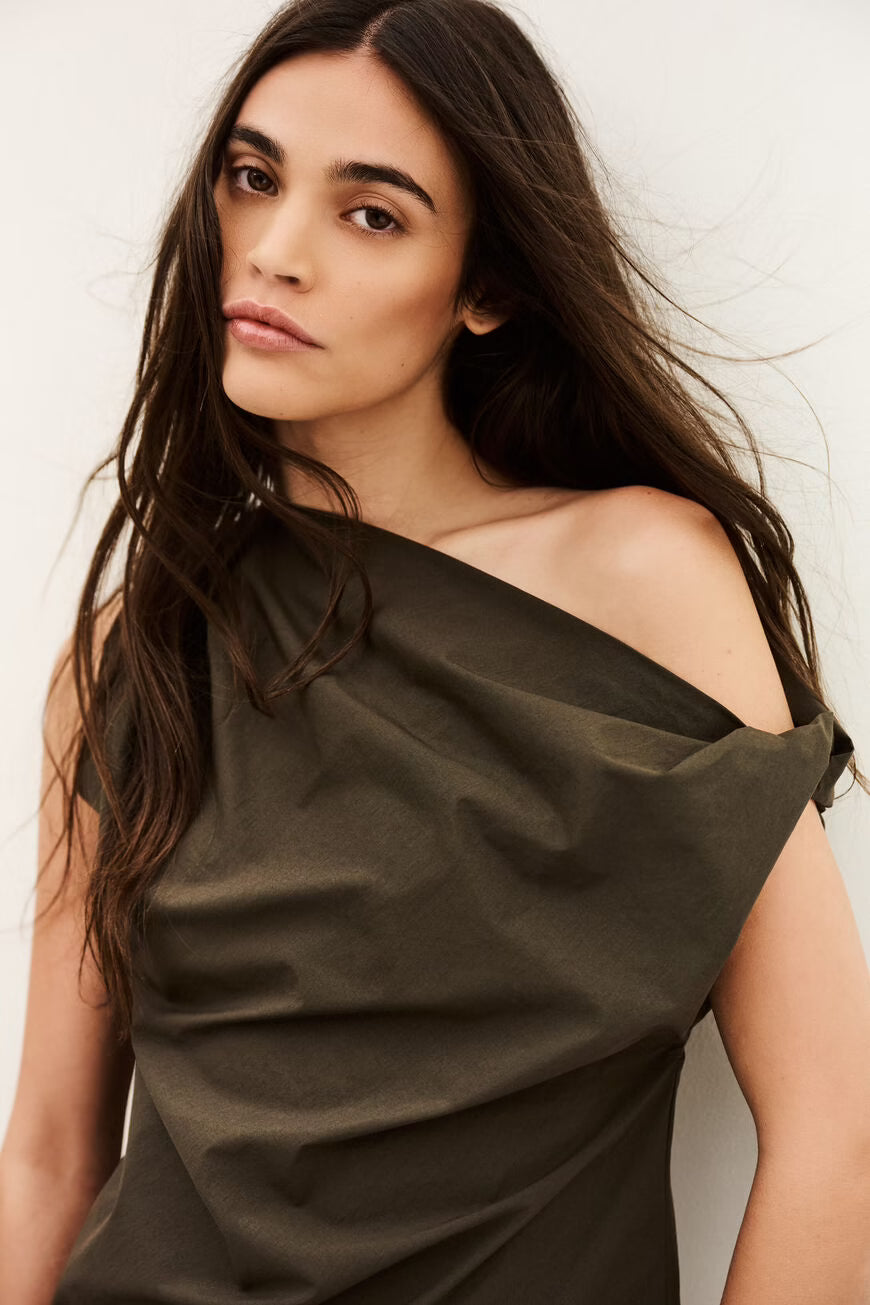 Woman wearing a dark green off-shoulder top against a plain background