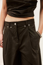 Person wearing black pants with silver buttons on a plain background