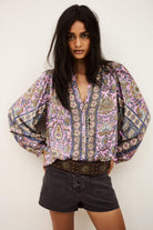 Woman wearing a patterned blouse and black shorts against a white background