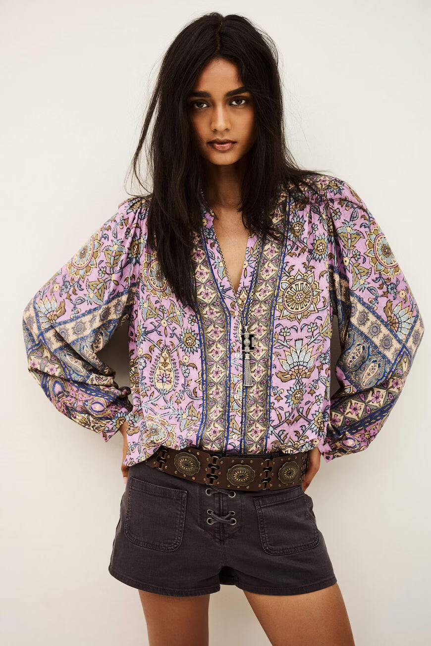 Woman wearing a patterned blouse and black shorts against a white background