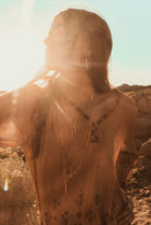 Woman with layered necklaces standing in a desert landscape with sunlight filtering through.