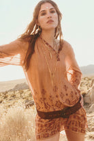 Woman in a patterned dress with long hair and layered necklaces standing in a desert landscape.