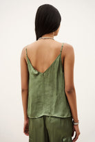 A woman shown from the back wearing an olive green satin camisole top with thin straps and a split V-back, paired with matching olive green pants, against a plain off-white background.