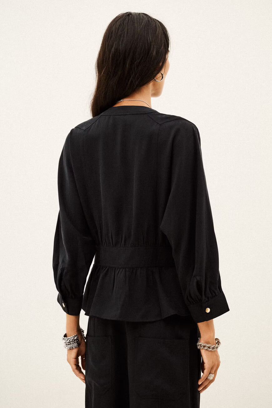 A woman shown from the back wearing a black long-sleeve blouse with a gathered waist and peplum hem, paired with black trousers, against a plain off-white background.