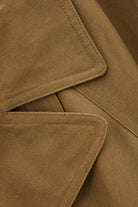 Close-up of a brown fabric garment showing the texture of the material and the details of the collar and pocket stitching.