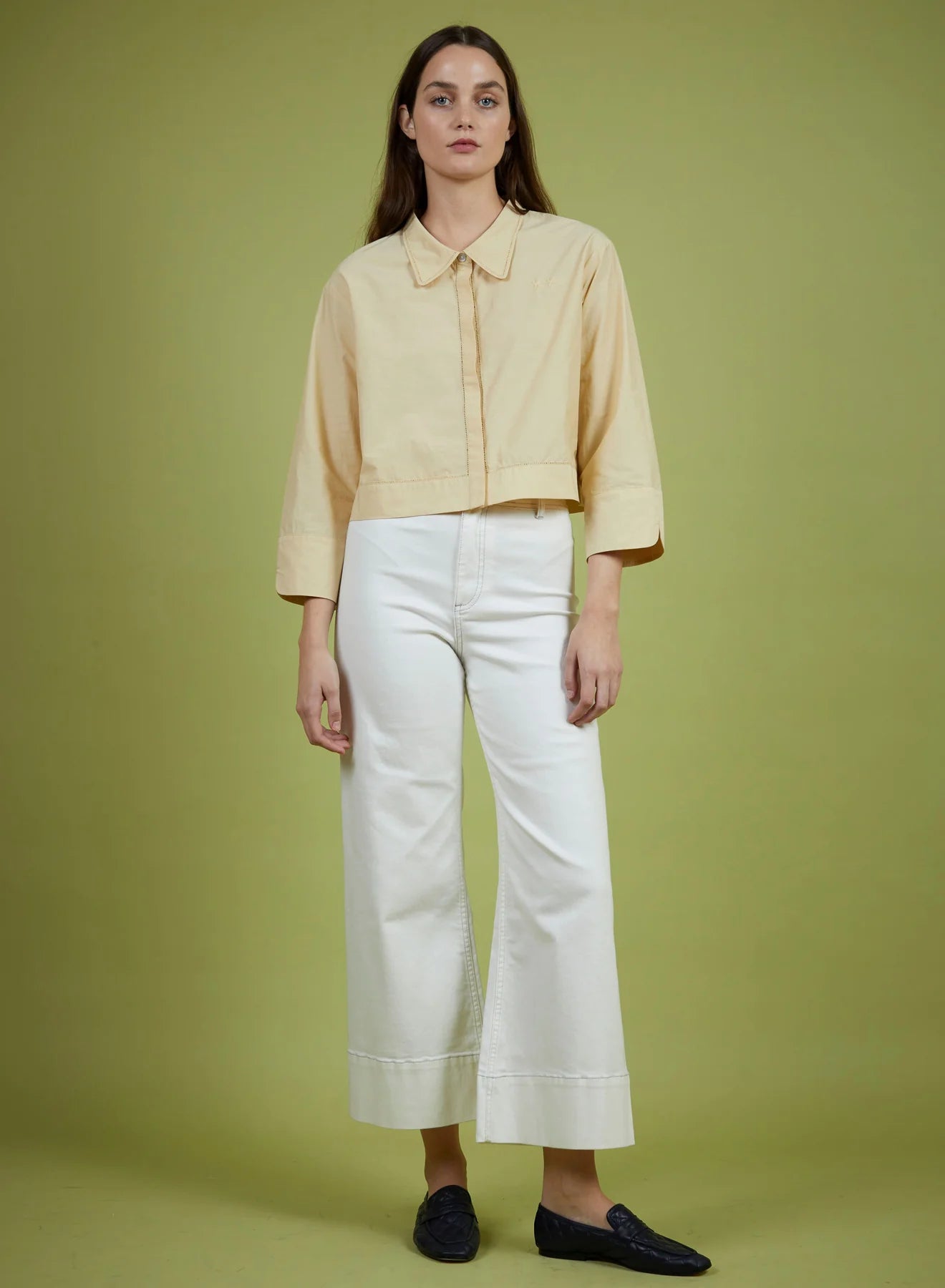 Woman wearing a light yellow blouse and white pants on a green background
