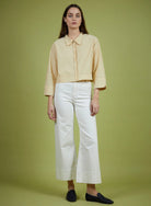 Woman wearing a light yellow blouse and white pants on a green background