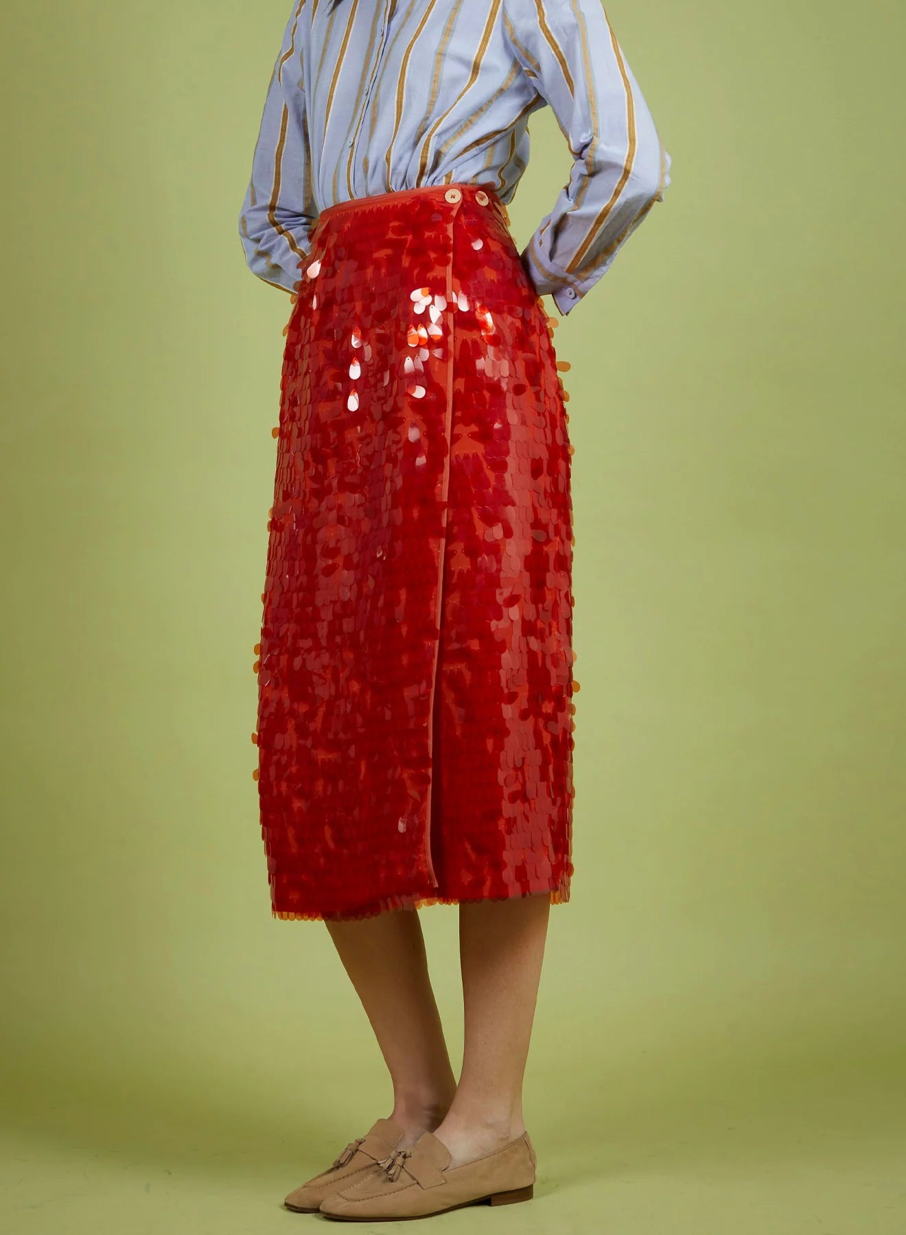 Person wearing a red sequin skirt with a light blue striped shirt on a green background