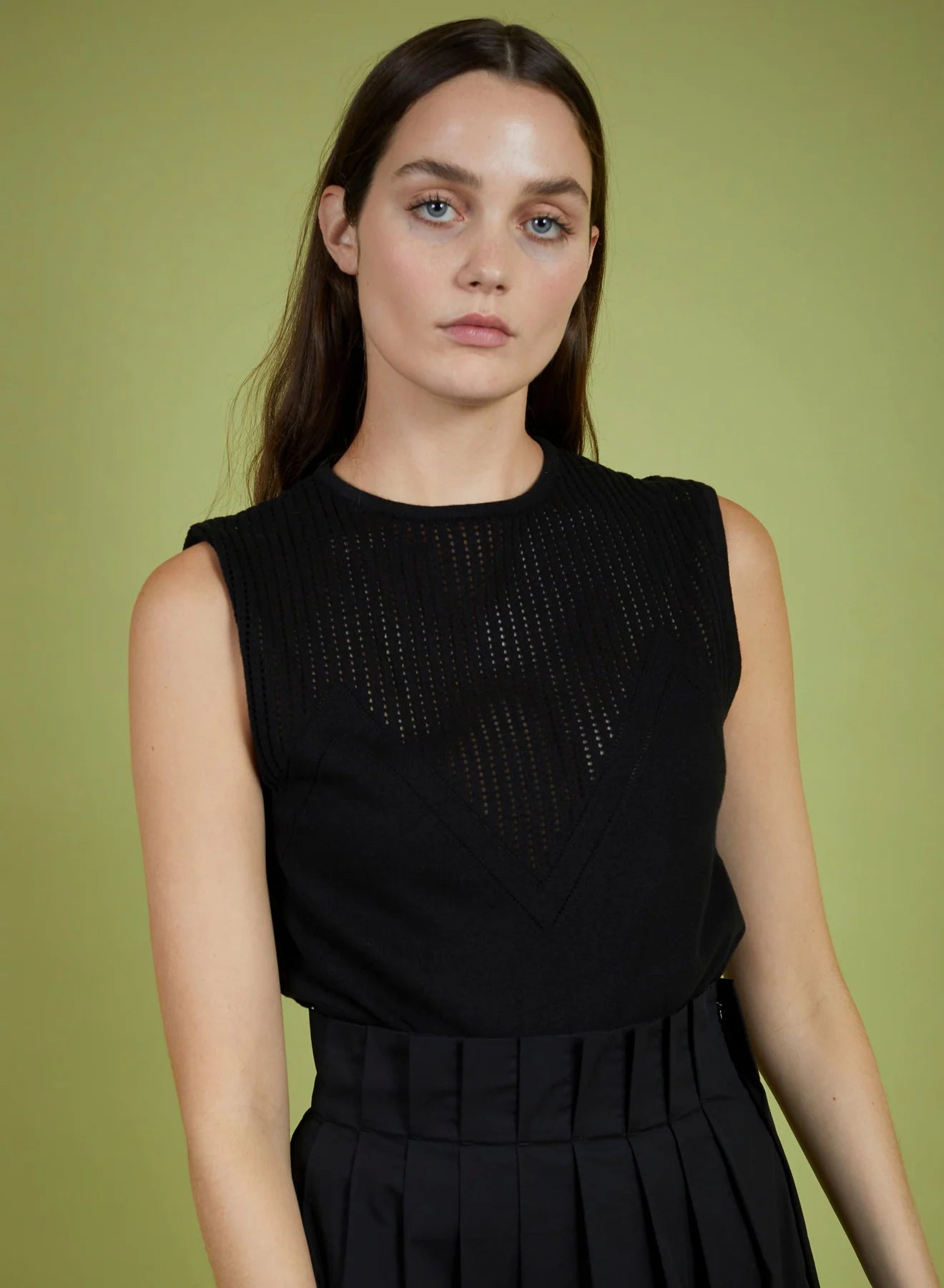 Woman wearing a black sleeveless top with a textured design against a green background