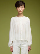 Woman wearing a white blouse and white pants against a green background