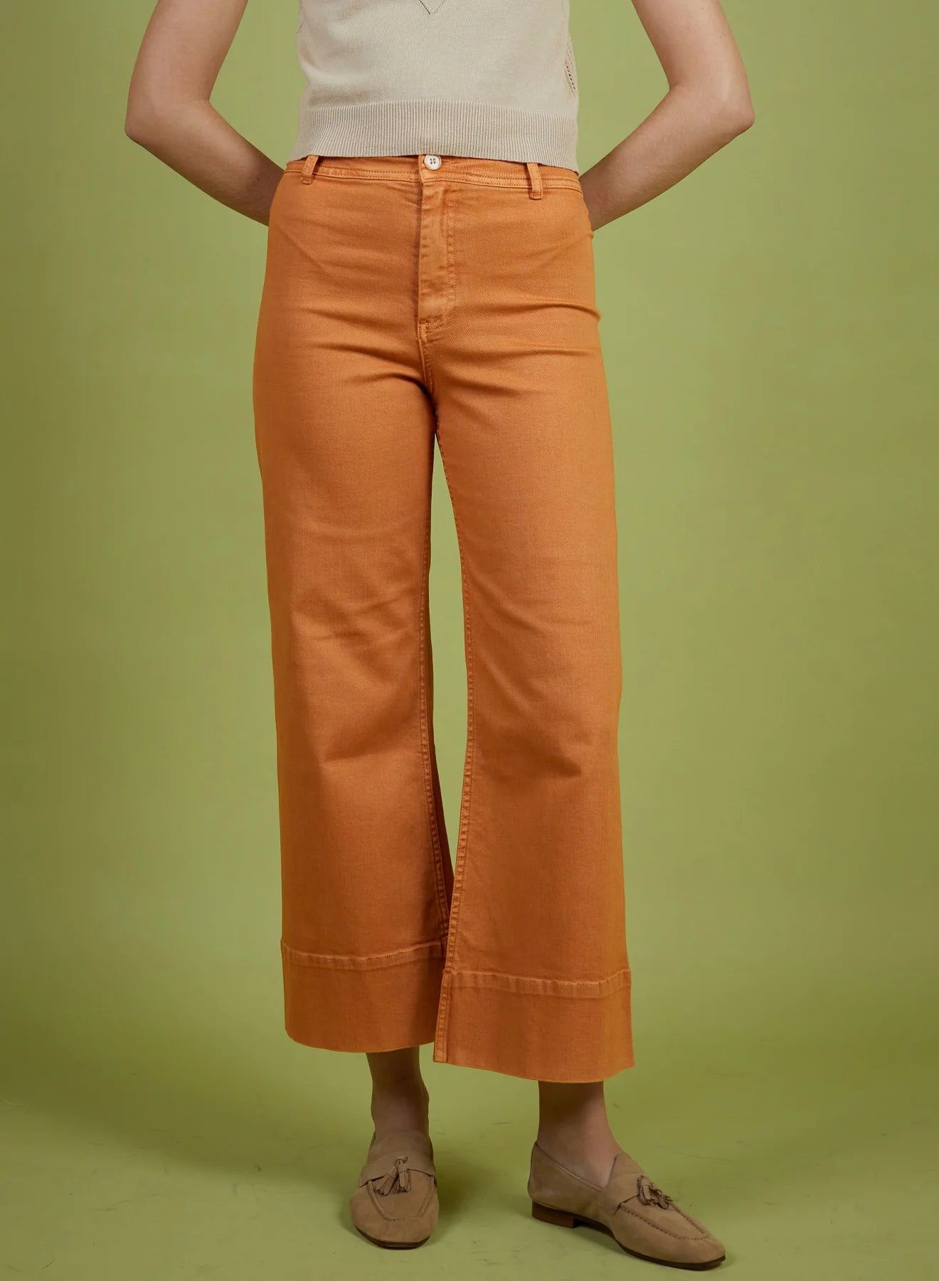 Person wearing orange pants and a light-colored top on a green background