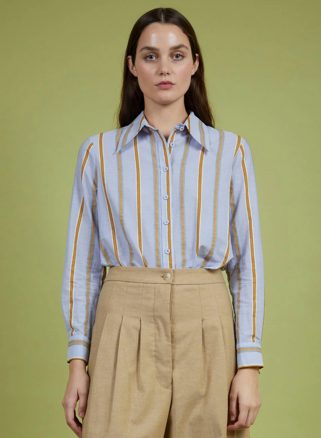 Woman wearing a striped shirt and beige pants against a green background