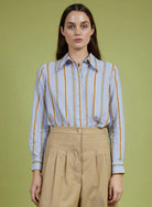 Woman wearing a striped shirt and beige pants against a green background