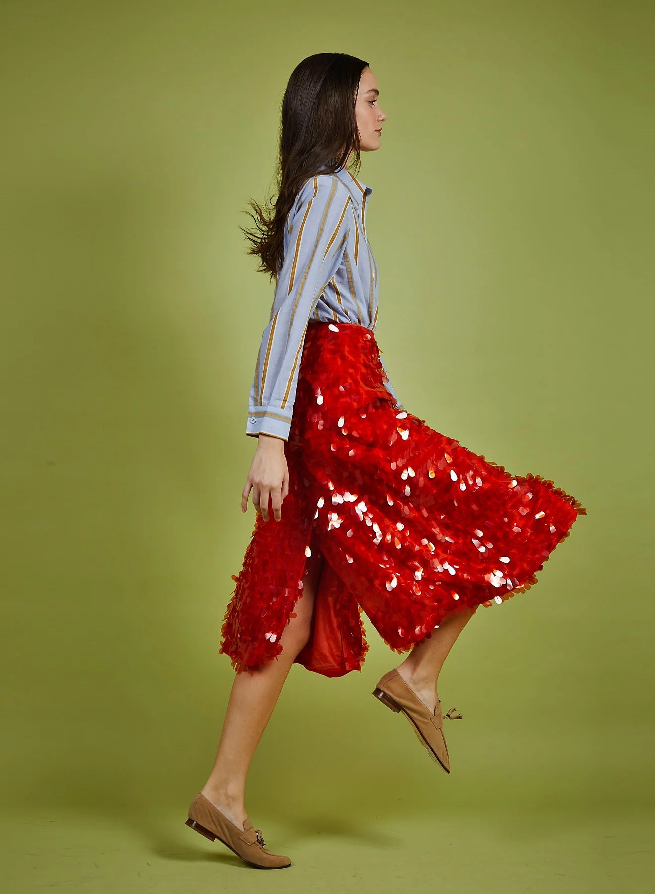 Woman wearing a red sequin skirt and striped shirt on a green background