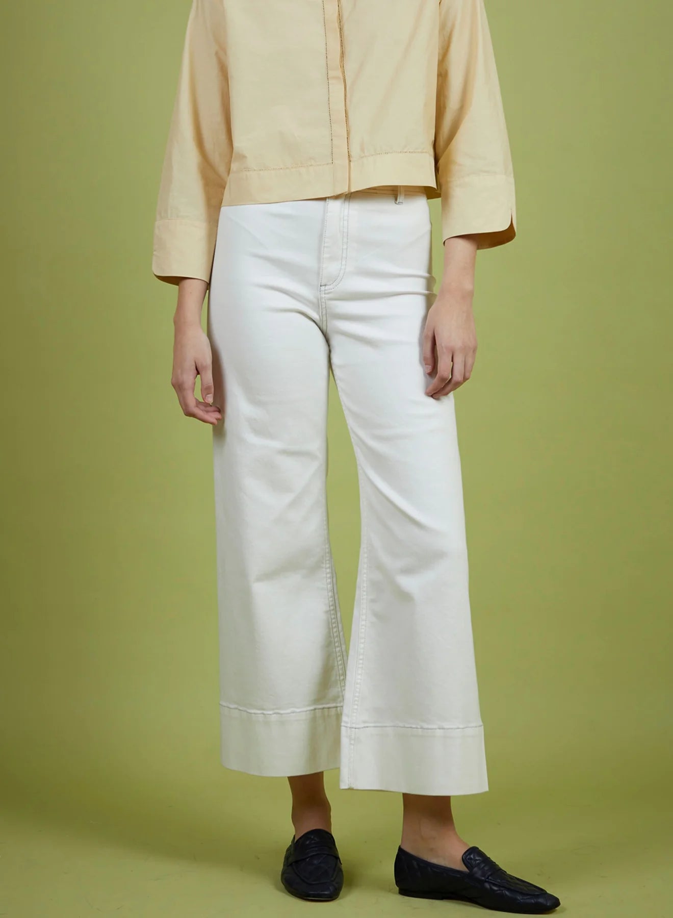 Person wearing a light yellow jacket and white pants on a green background