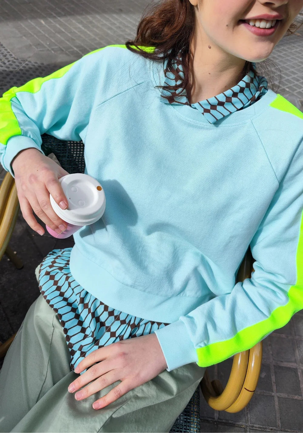 Person wearing a light blue sweatshirt with green accents, sitting outdoors.