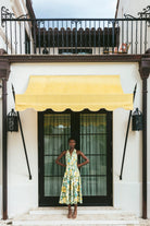 Woman in a floral dress standing in front of a white building with a yellow awning.