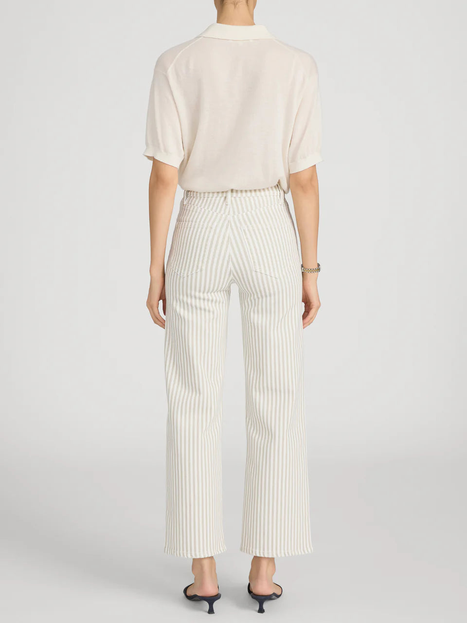 Person wearing a cream-colored blouse and striped pants on a light gray background