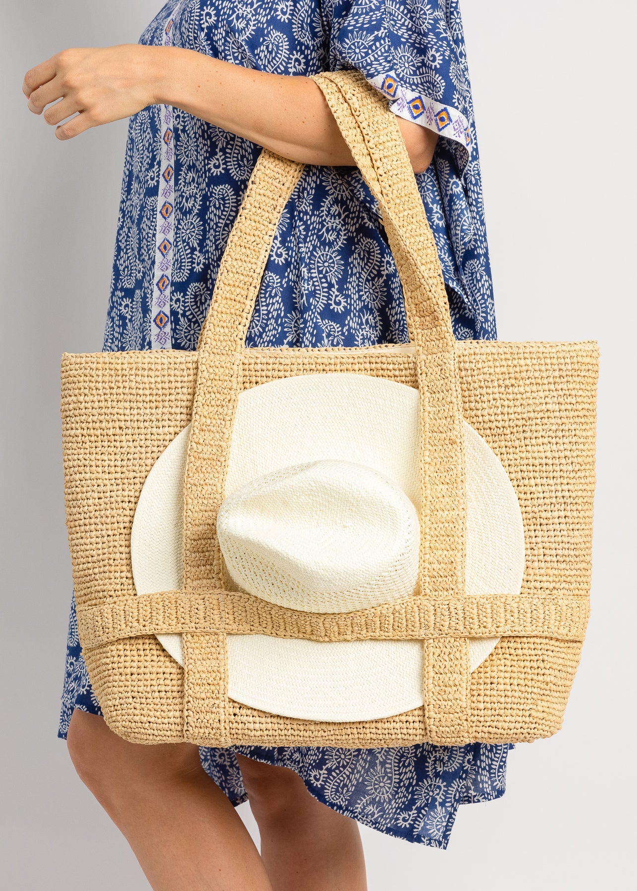 Person holding a straw bag with a white hat inside, wearing a blue floral dress.