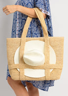 Person holding a straw bag with a white hat inside, wearing a blue floral dress.