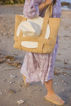 Person holding a woven bag with a white hat on a sandy beach