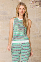 Woman wearing a sleeveless top and pants with a zigzag pattern against a stone wall.