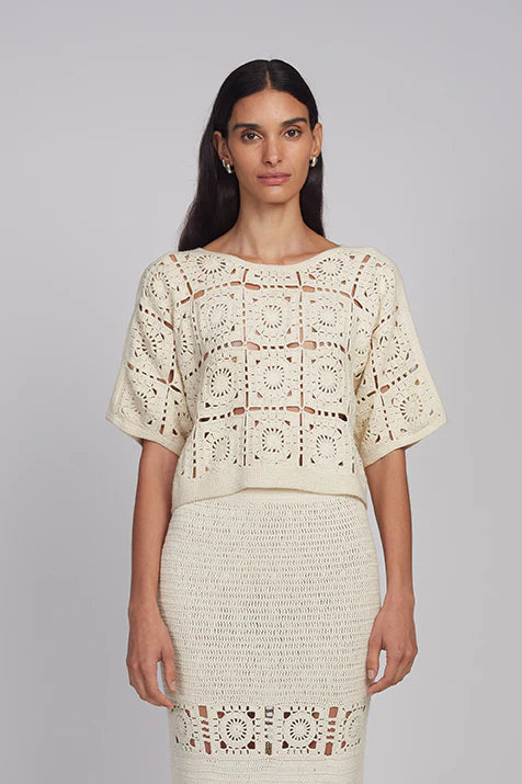 Woman wearing a beige crochet top and skirt on a gray background